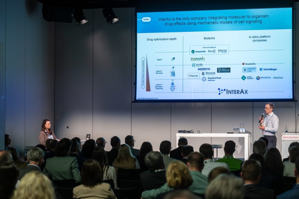 Presenter on stage with a company slide at the Swiss Biotech Day 2026