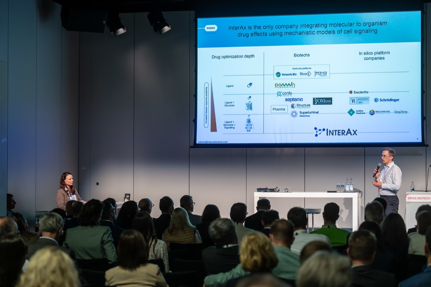 Presenter on stage with a company slide at the Swiss Biotech Day 2026