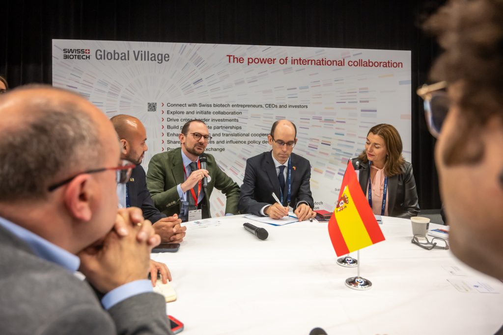 A roundtable in the Global Village at the Swiss Biotech Day 2025, a Spanish flag on the table and the words The power of international collaboration on the wall behind