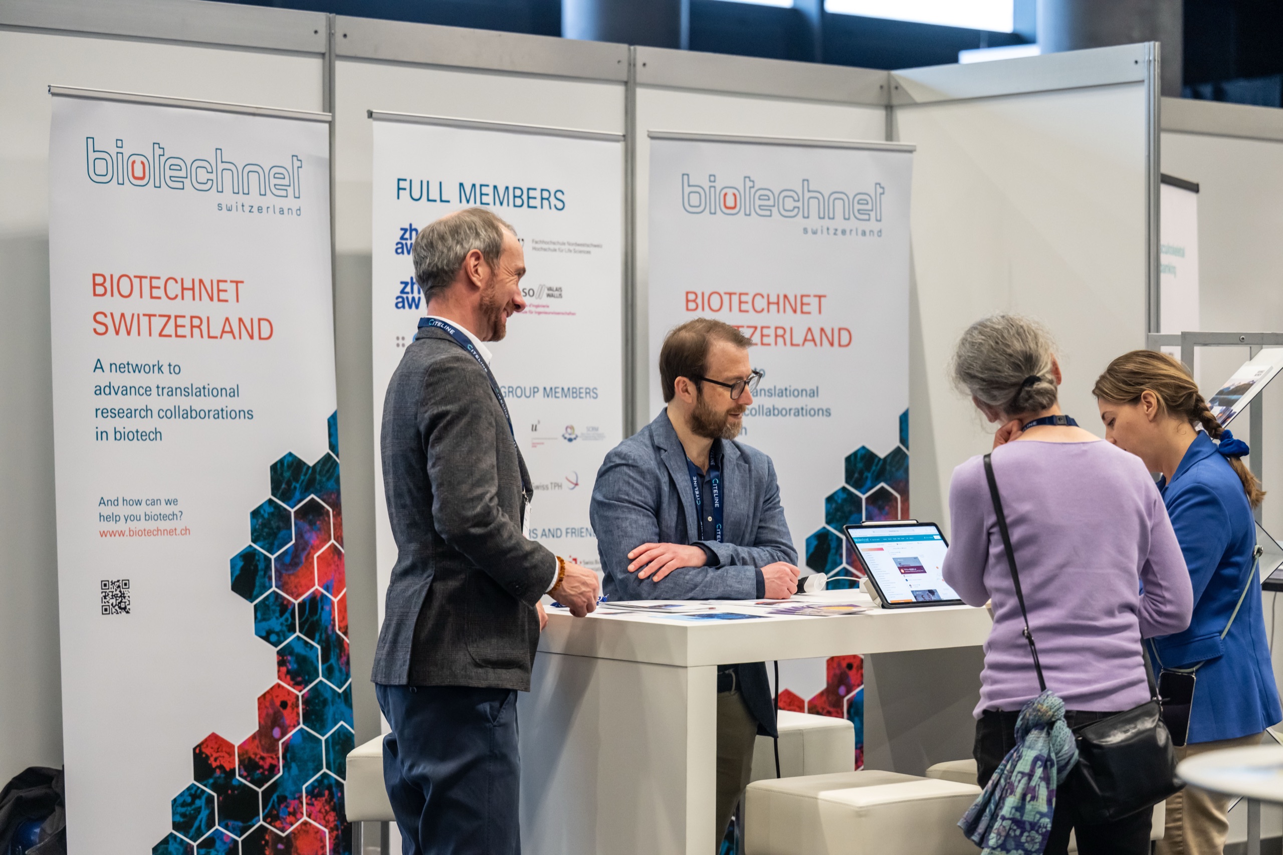 Two visitors in conversation with the Biotechnet Switzerland team at their Swiss cluster booth at the Swiss Biotech Day 2026